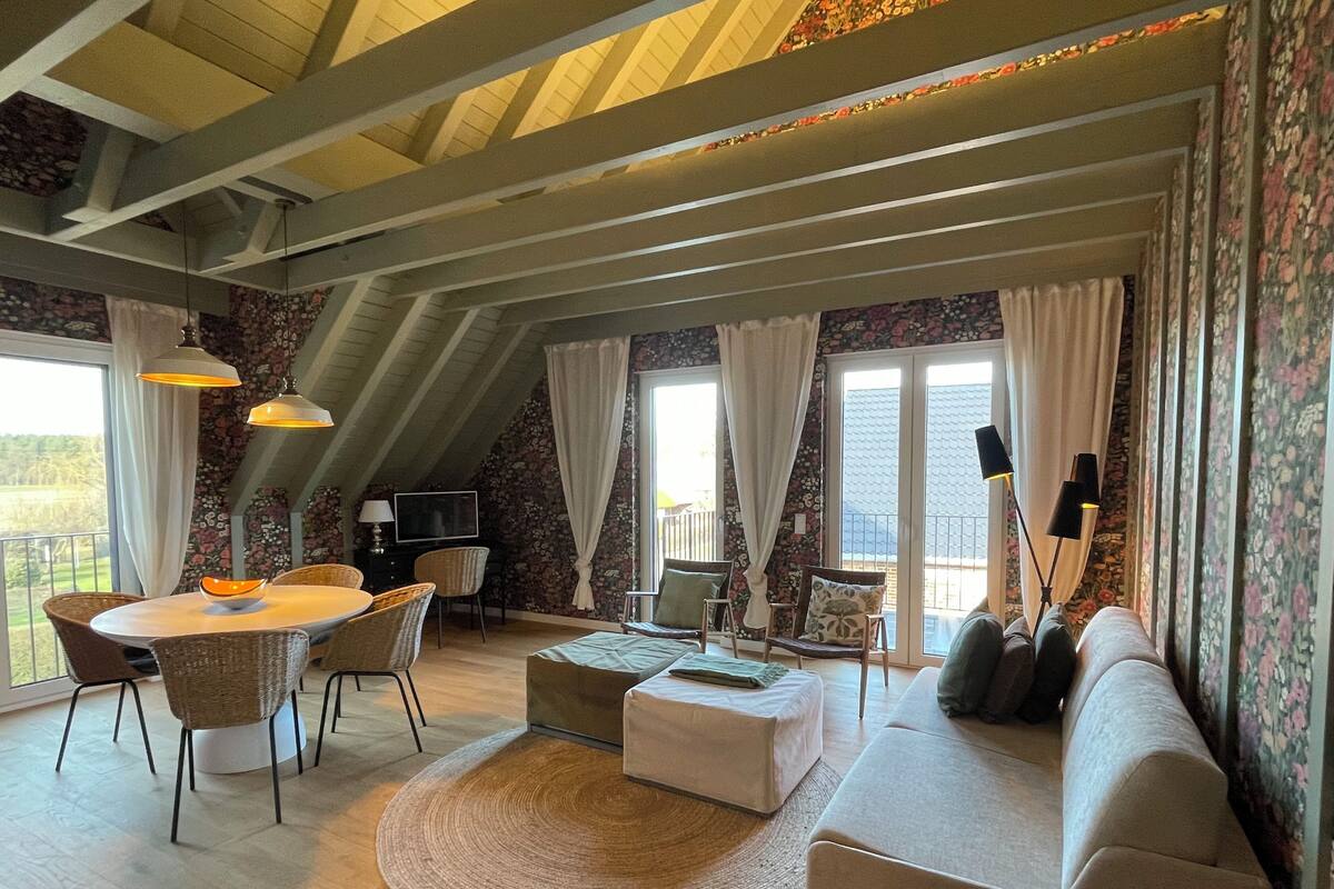 Un salon spacieux avec un plafond haut, un coin repas avec des chaises en osier, un canapé et un téléviseur.