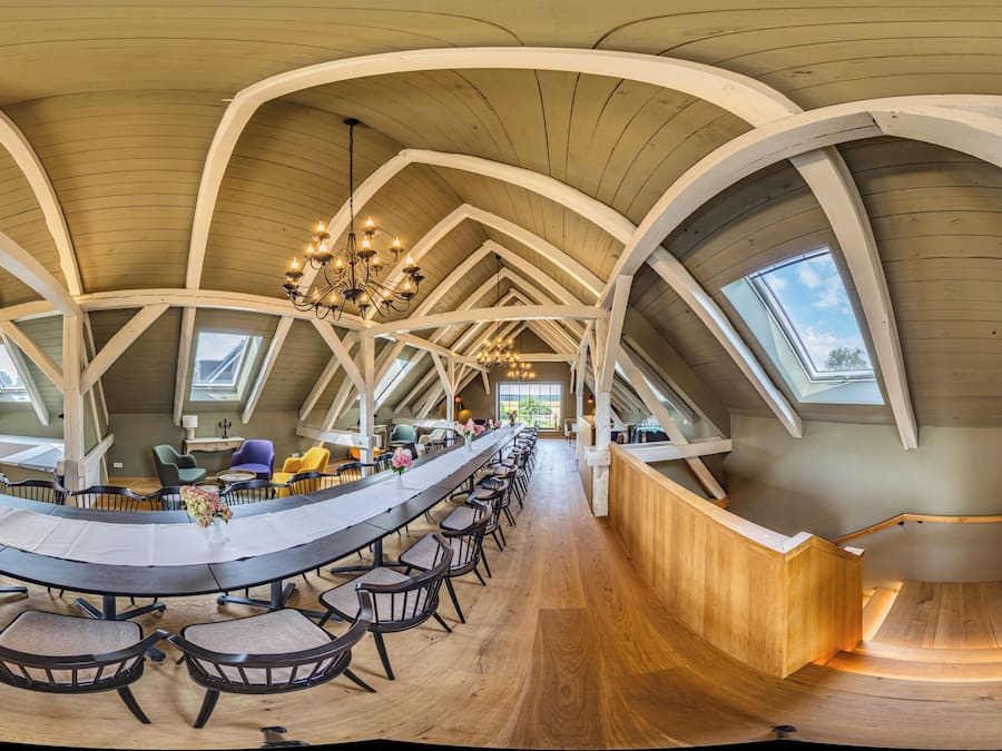 Ein geräumiger Saal mit langem Tisch und Stühlen, hohen Holzbalkendecken und Oberlichtern.