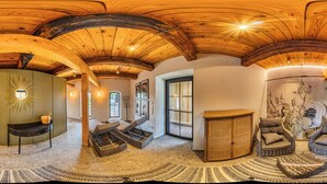 Una habitación amplia con alto techo de madera, un gran ventanal, una silla de mimbre, una cesta tejida y un tapete estampado.