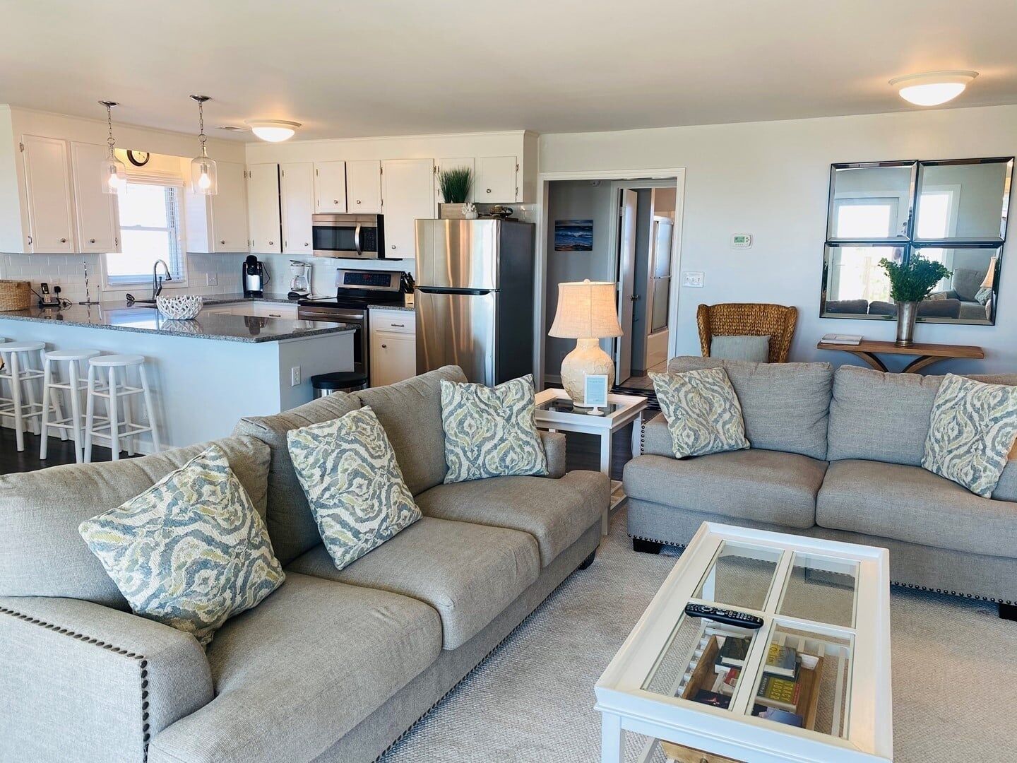 A modern living room with a grey sofa set, a coffee table, and a kitchen area with stainless steel appliances.