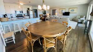A modern kitchen with a central island, dining area with a round table and chairs, and a living room with a sofa and television.