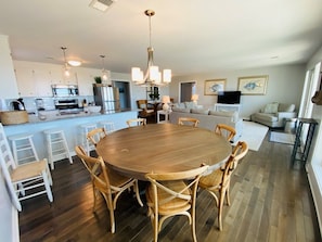 A modern kitchen with a central island, dining area with a round table and chairs, and a living room with a sofa and television.