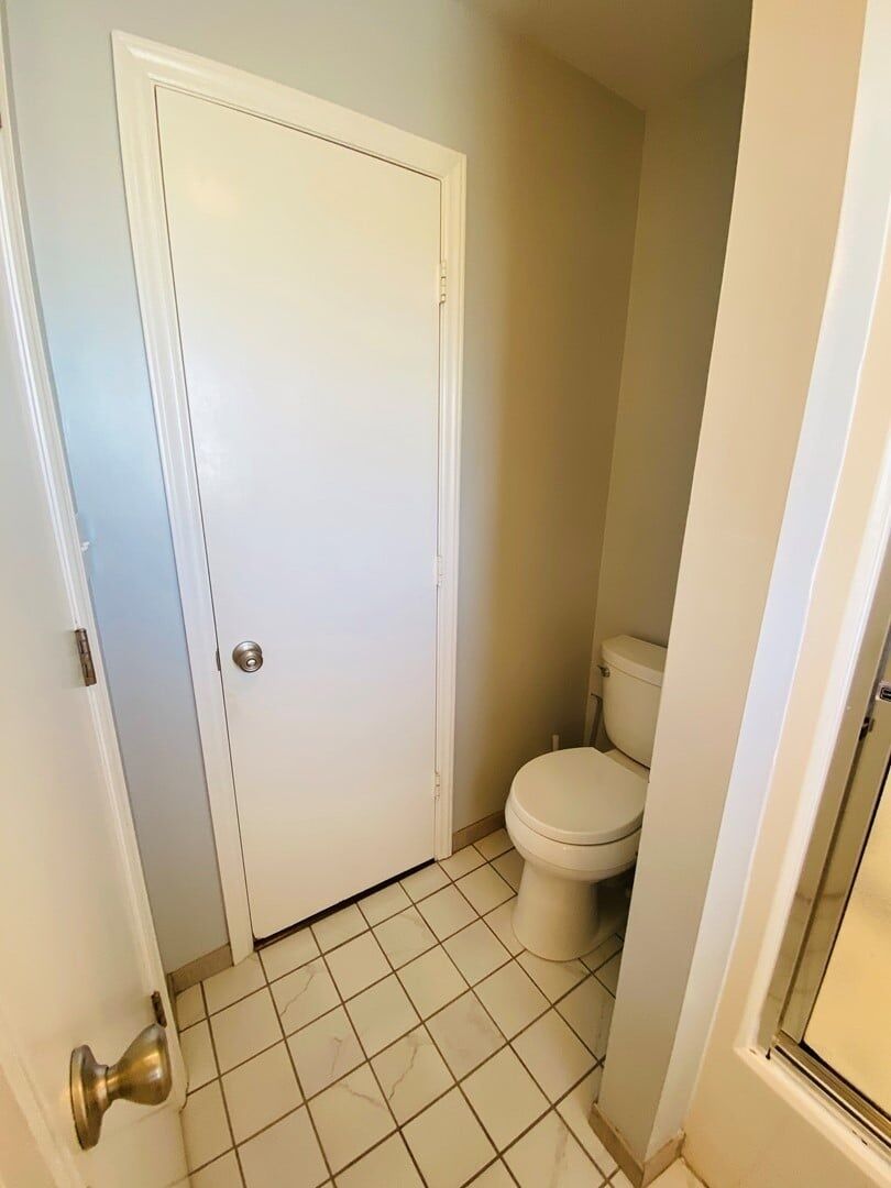 Ein kleines, sauberes Badezimmer mit Toilette, weißer Tür und gefliestem Boden.