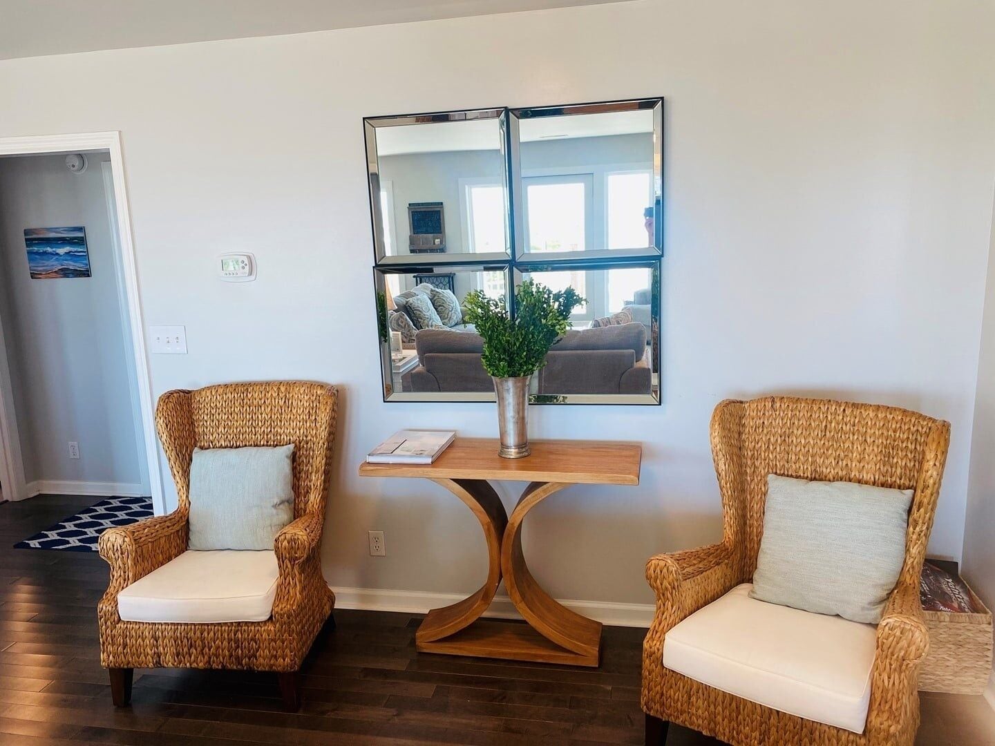 Ein Zimmer mit zwei Korbstühlen, einem Holztisch mit einer Vase und einem großen Spiegel an der Wand.