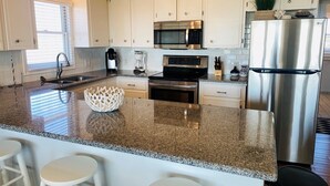 A modern kitchen with white cabinets, stainless steel appliances, granite countertops, and bar stools.