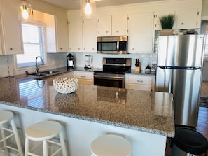 A modern kitchen with white cabinets, stainless steel appliances, granite countertops, and bar stools.