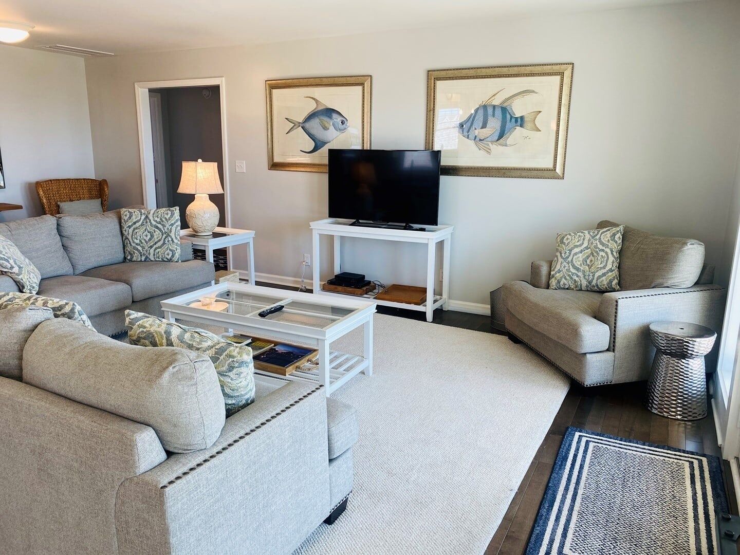 A living room with a sofa, coffee table, TV, and framed fish paintings on the wall.