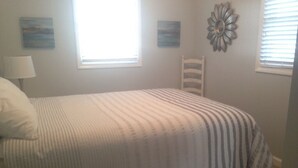 A bedroom with a bed, a chair, two windows, and wall art.