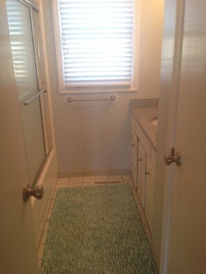 A narrow bathroom with a window, a towel rack, a green rug, and a door. - Dune Deck South -  4 Bedroom Home by RedAwning (Supply)