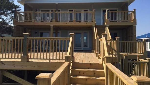 A two-story building with a balcony on the upper floor, a wooden deck with stairs, and a clear sky.