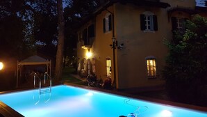 Une piscine dotée d’une terrasse en bois et de rampes en métal, entourée d’une pelouse bien entretenue et d’arbres.
