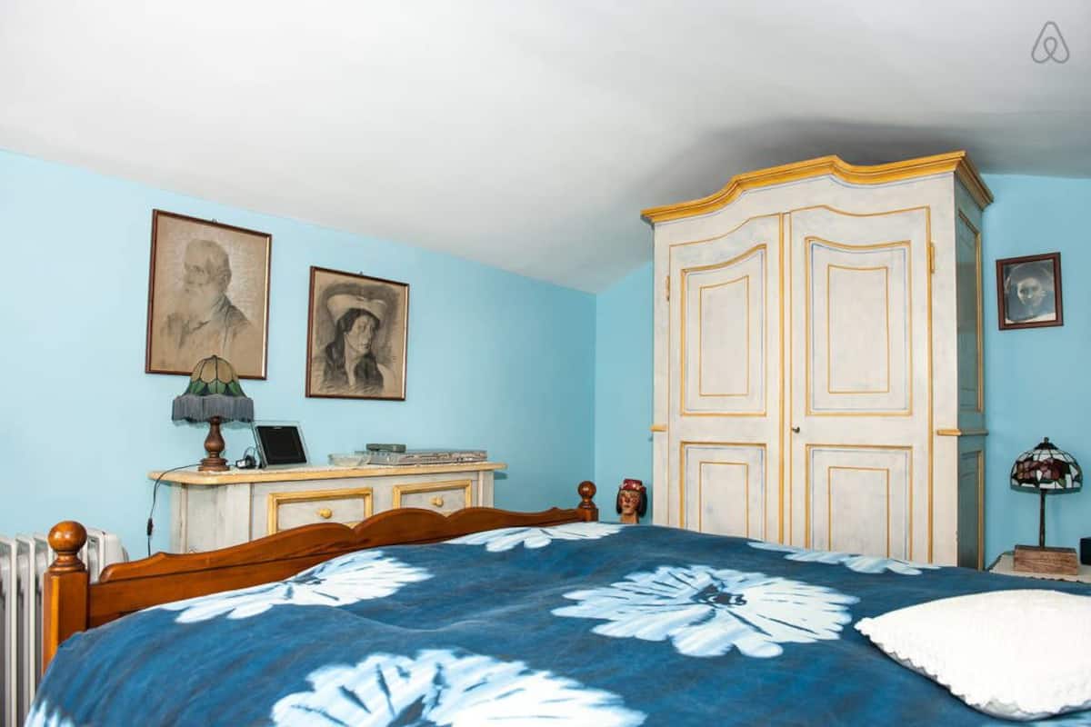A bedroom with a bed, a dresser, a wardrobe, and two framed portraits on the wall.
