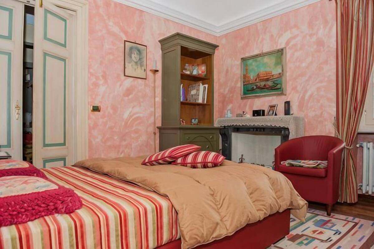 A bedroom with a bed, a red armchair, a fireplace, and a wardrobe.