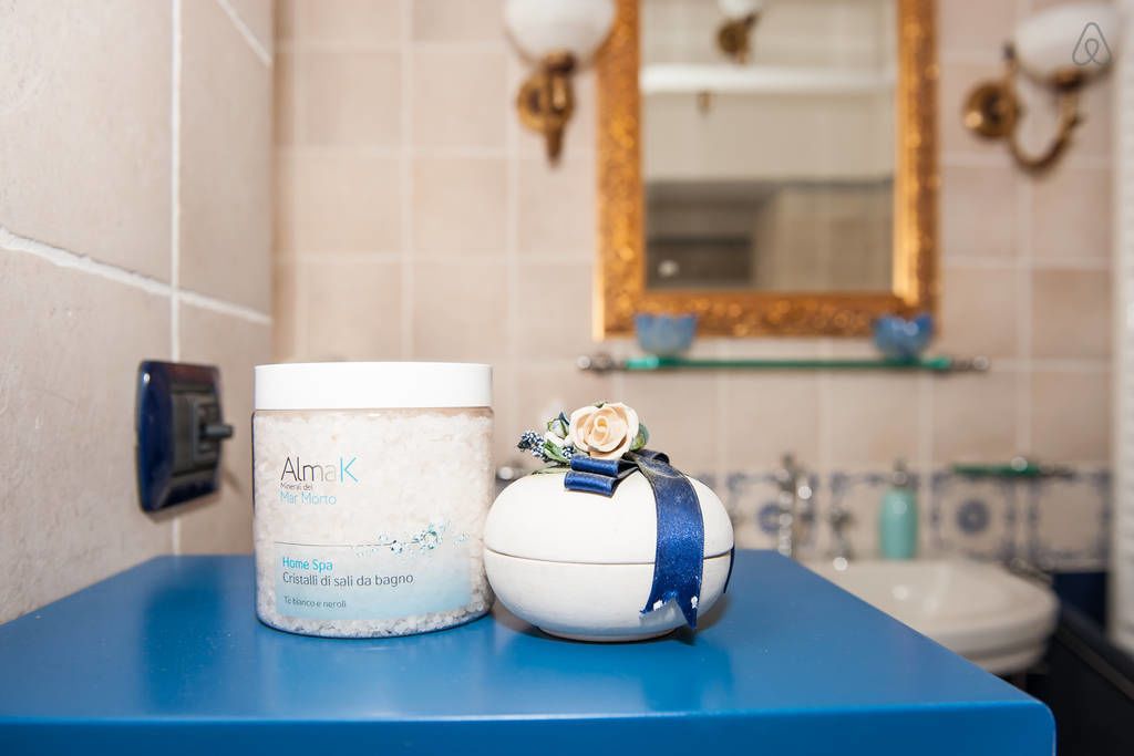 Ein Badezimmer mit blauer Ablage, einem weißen Behälter mit der Aufschrift 'AlmaK Home Spa' und einem dekorativen weißen Ei mit blauem Band und einer Blume.