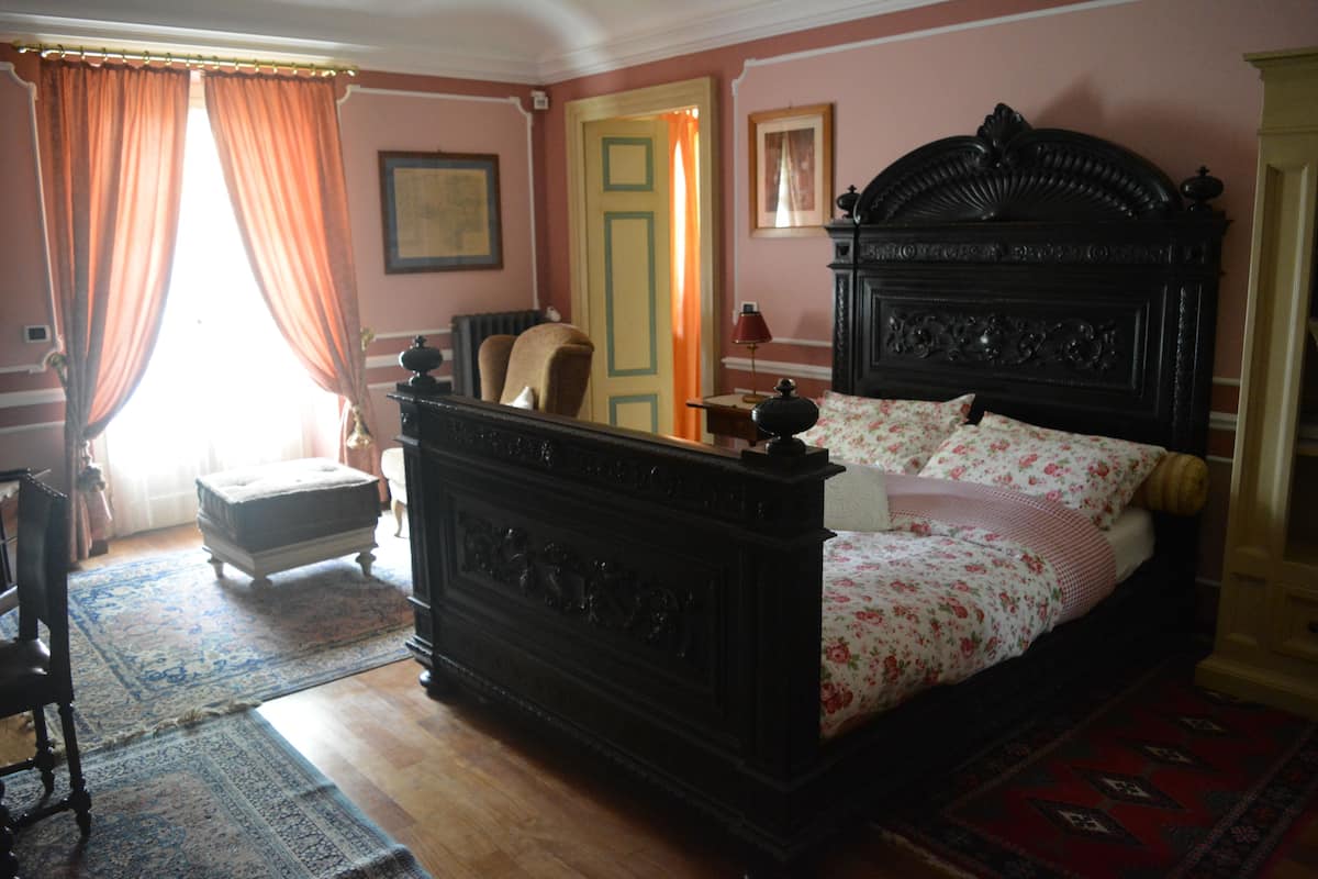 A traditional bedroom with a four-poster bed, a wooden floor, and a large window with curtains.