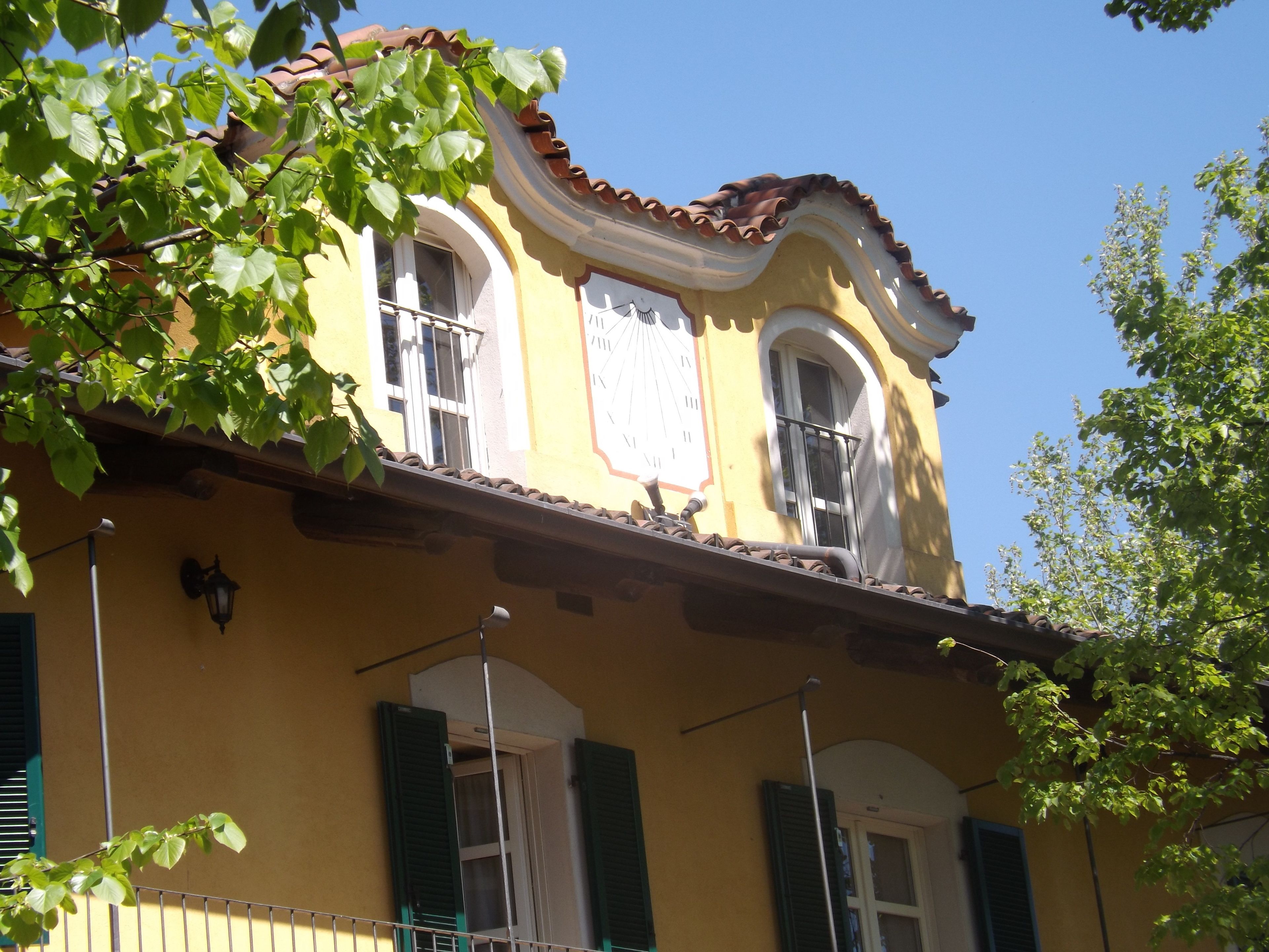 Un edificio amarillo con contraventanas verdes, un reloj y un balcón.