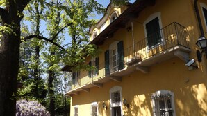 Un bâtiment jaune doté d’un balcon, de plantes en pot et d’un arbre aux fleurs violettes.