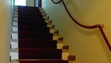 Un escalier dont les marches sont recouvertes d’une moquette rouge et qui est délimité par une cordelette rouge.