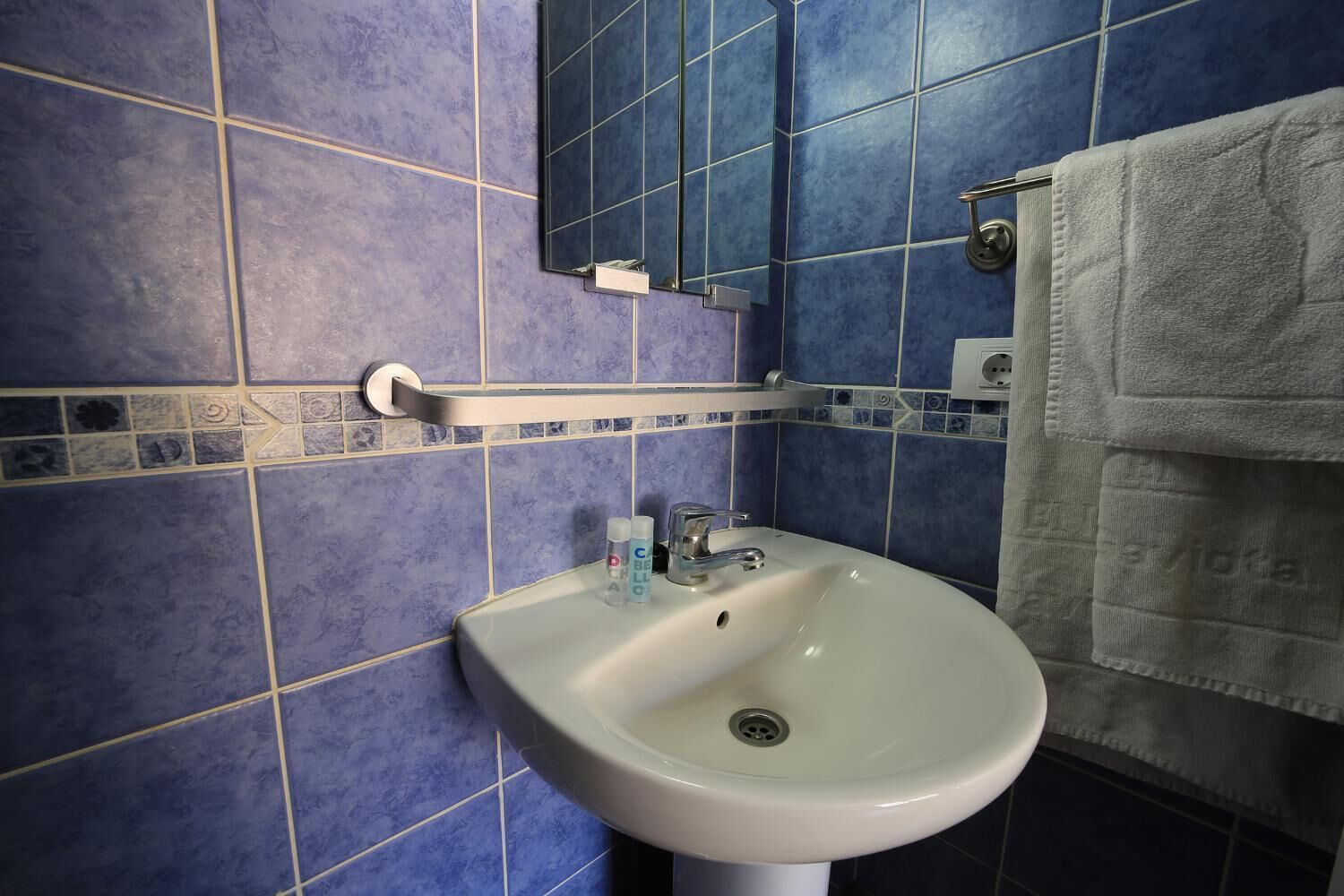 A bathroom with a white sink, blue tiles, a towel rack, and a mirror.