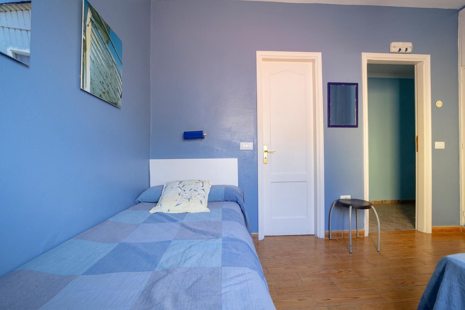 A bedroom with a bed, a nightstand, a chair, and a door leading to another room.