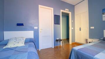 Habitación de hotel con dos camas, un taburete pequeño y un armario.