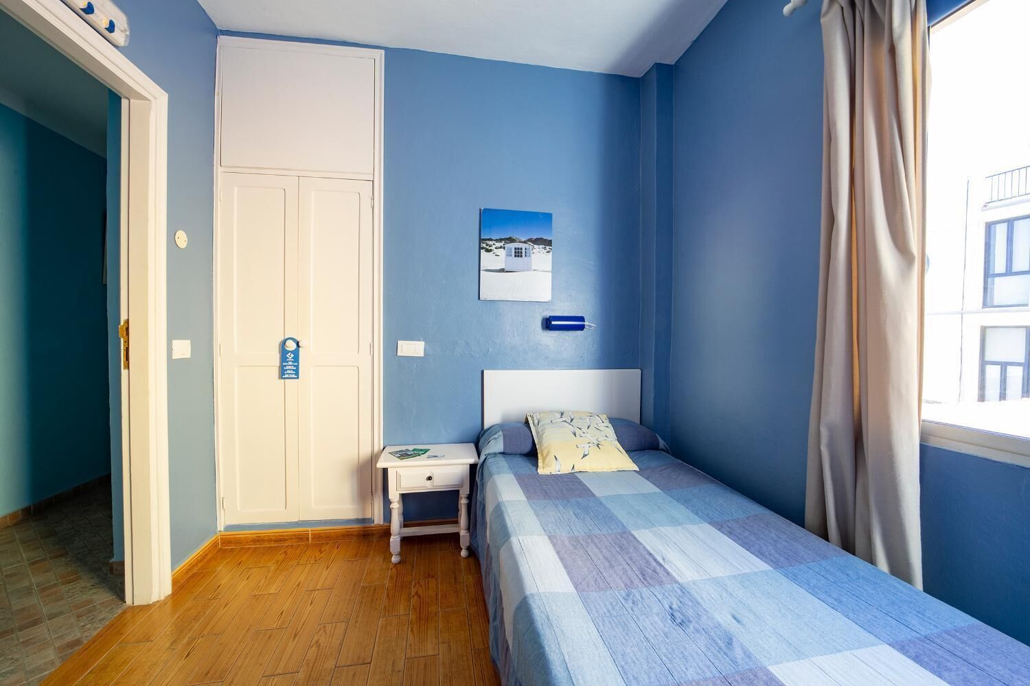 Un dormitorio con cama, mesita de noche, puerta y ventana con cortinas.