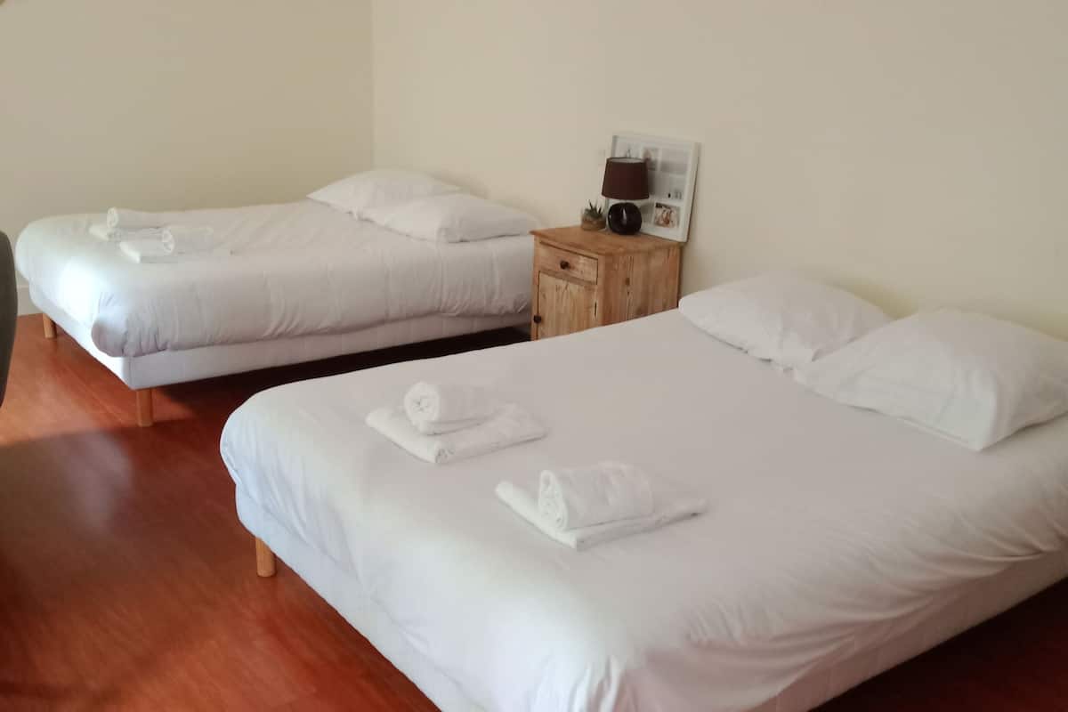 Two single beds with white linens and towels, a wooden nightstand with a lamp, and a wooden floor.