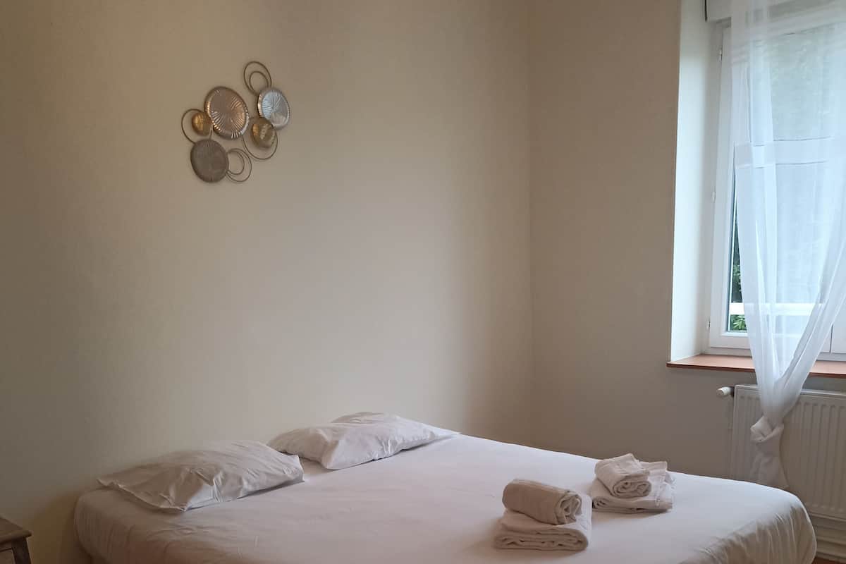 A neatly made bed with white linens and rolled towels, a wooden nightstand, and a wall-mounted decorative plate.