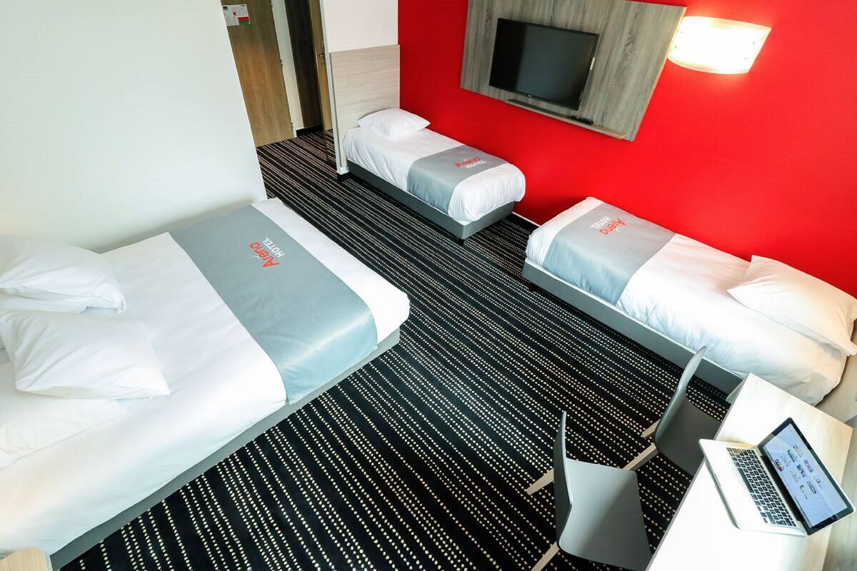 Ein Hotelzimmer mit zwei Einzelbetten, einem Schreibtisch mit einem Laptop und einem an der Wand befestigten Fernseher.