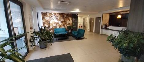 Un hall d’entrée spacieux au design moderne, agrémenté d’un mur à motifs, de deux canapés bleus et de plusieurs plantes en pot.
