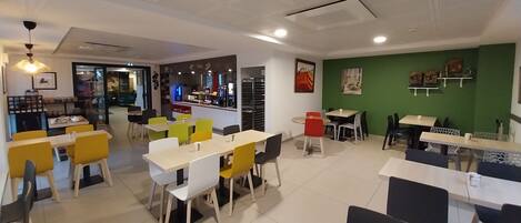 A modern cafe with multiple seating areas, including tables and chairs, and a visible counter with a coffee machine.