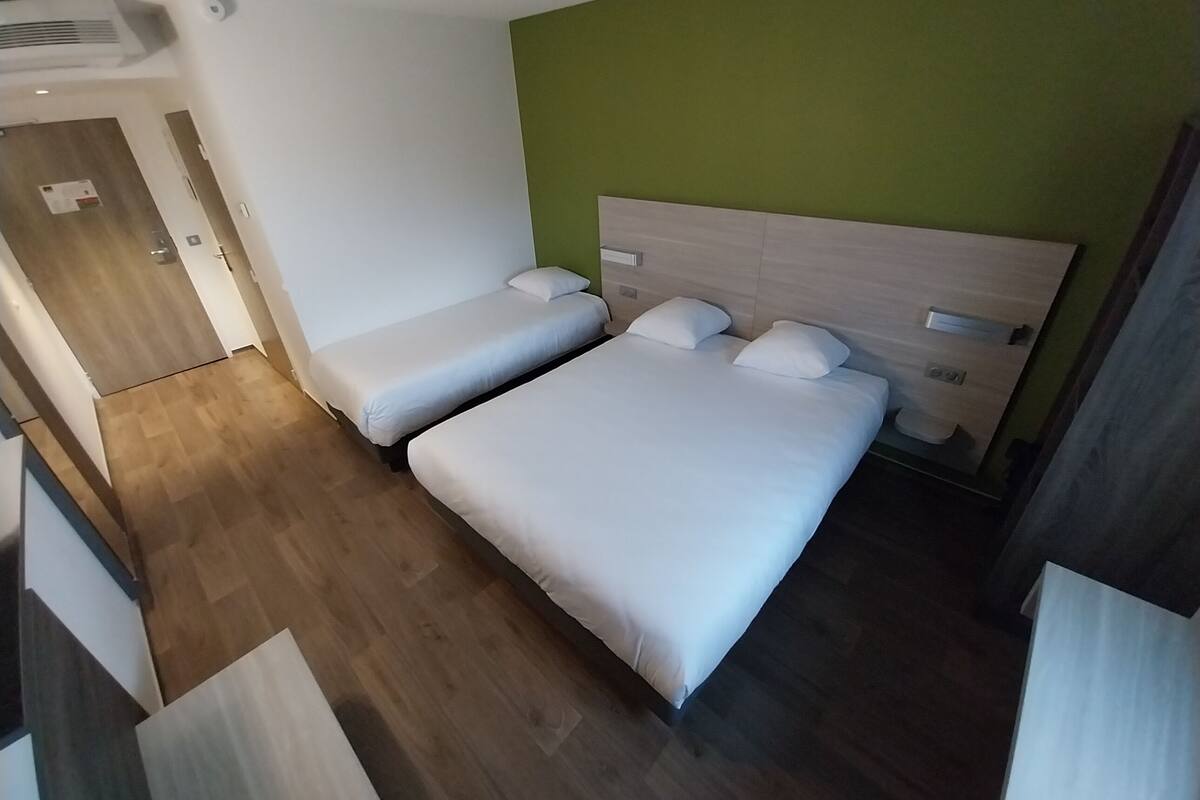 Ein Hotelzimmer mit zwei Einzelbetten, einem Holzkopfstück, einer grünen Akzentwand und einem Holzboden.