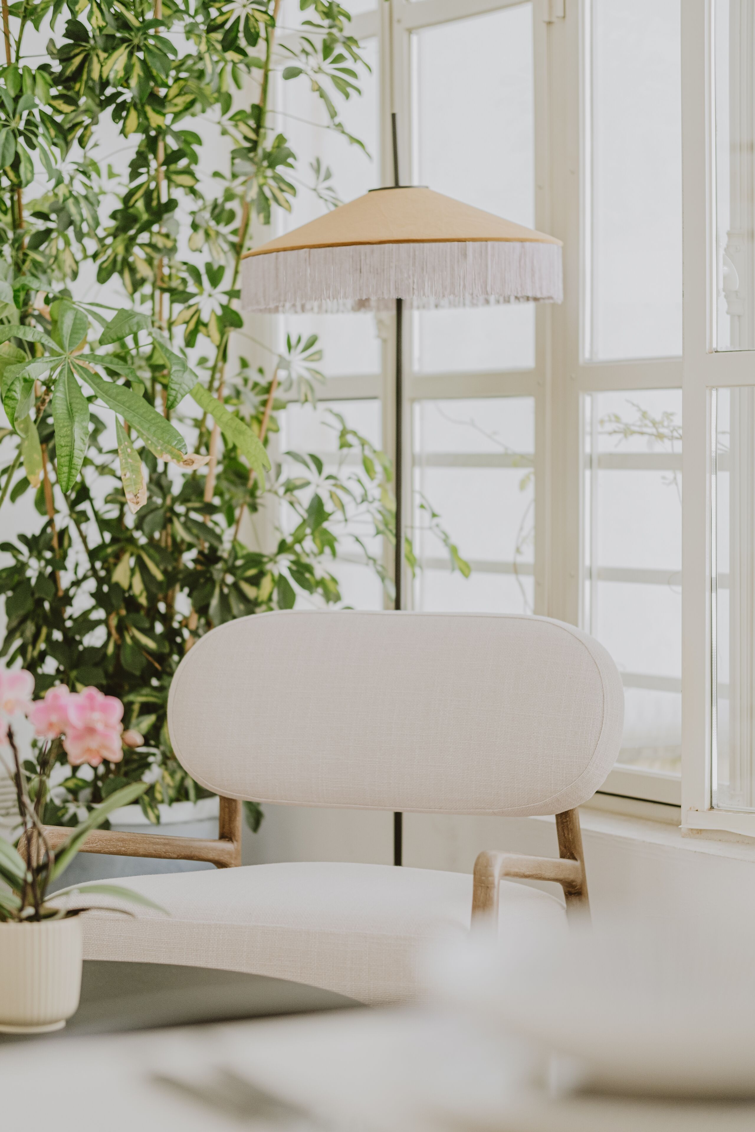 A room with a white chair, a hanging lamp, and a large window with a view of greenery.