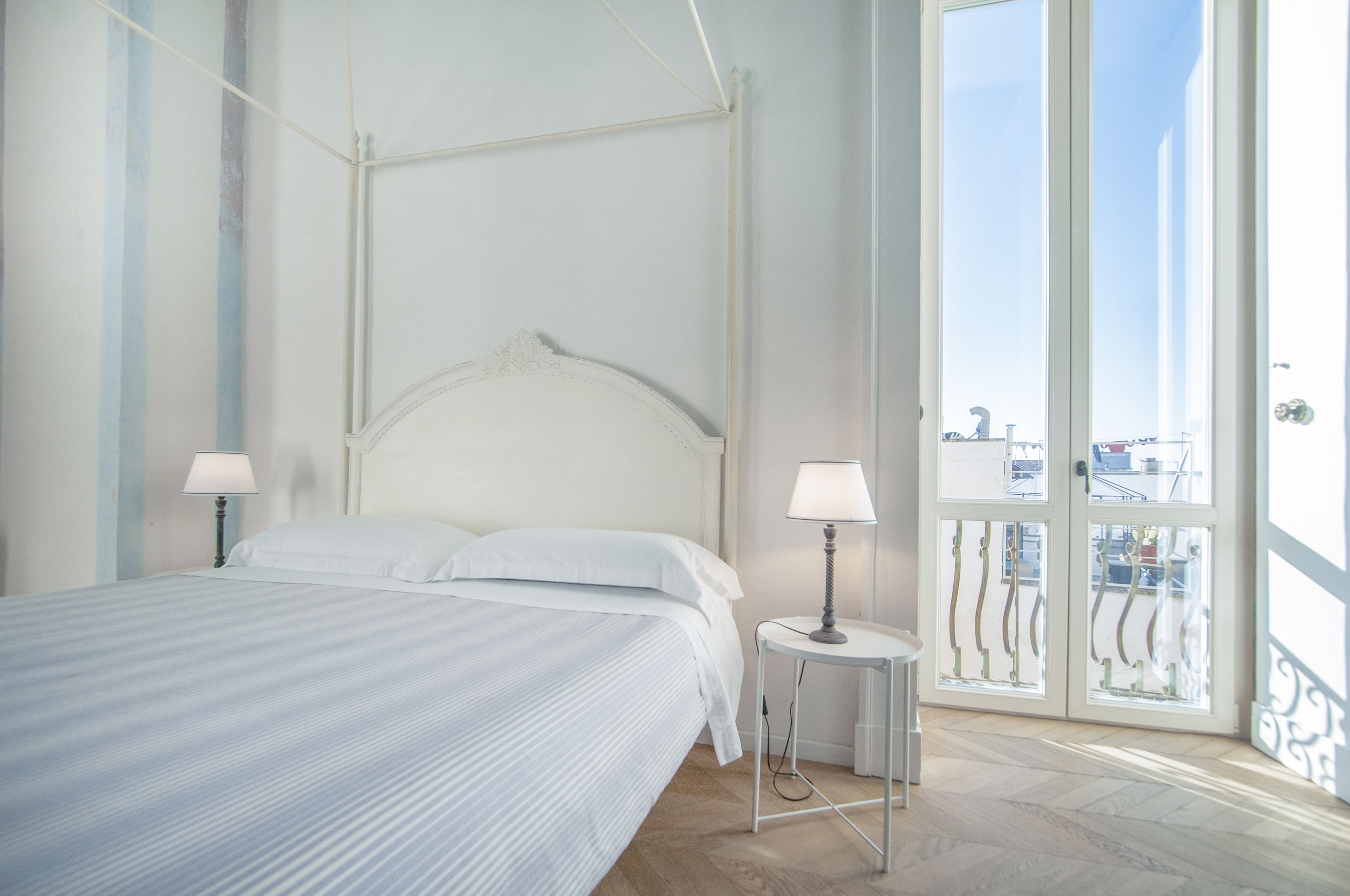 Een netjes opgemaakt bed met een hoofdeinde, twee bedlampen en een balkon met een hekwerk.