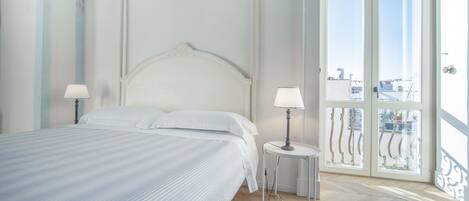A neatly made bed with a headboard, two bedside lamps, and a balcony with a railing.