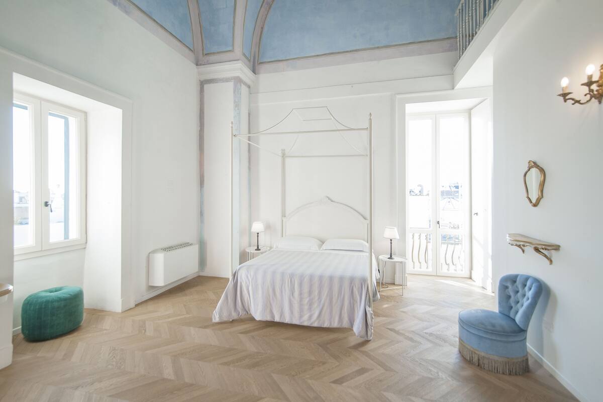 Una camera da letto con un letto grande, una piccola sedia, un comodino e un termosifone.