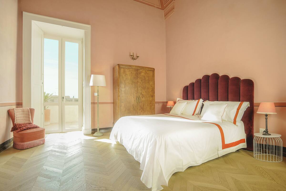Una camera d'albergo con un letto grande, un armadio in legno, una sedia e una lampada.