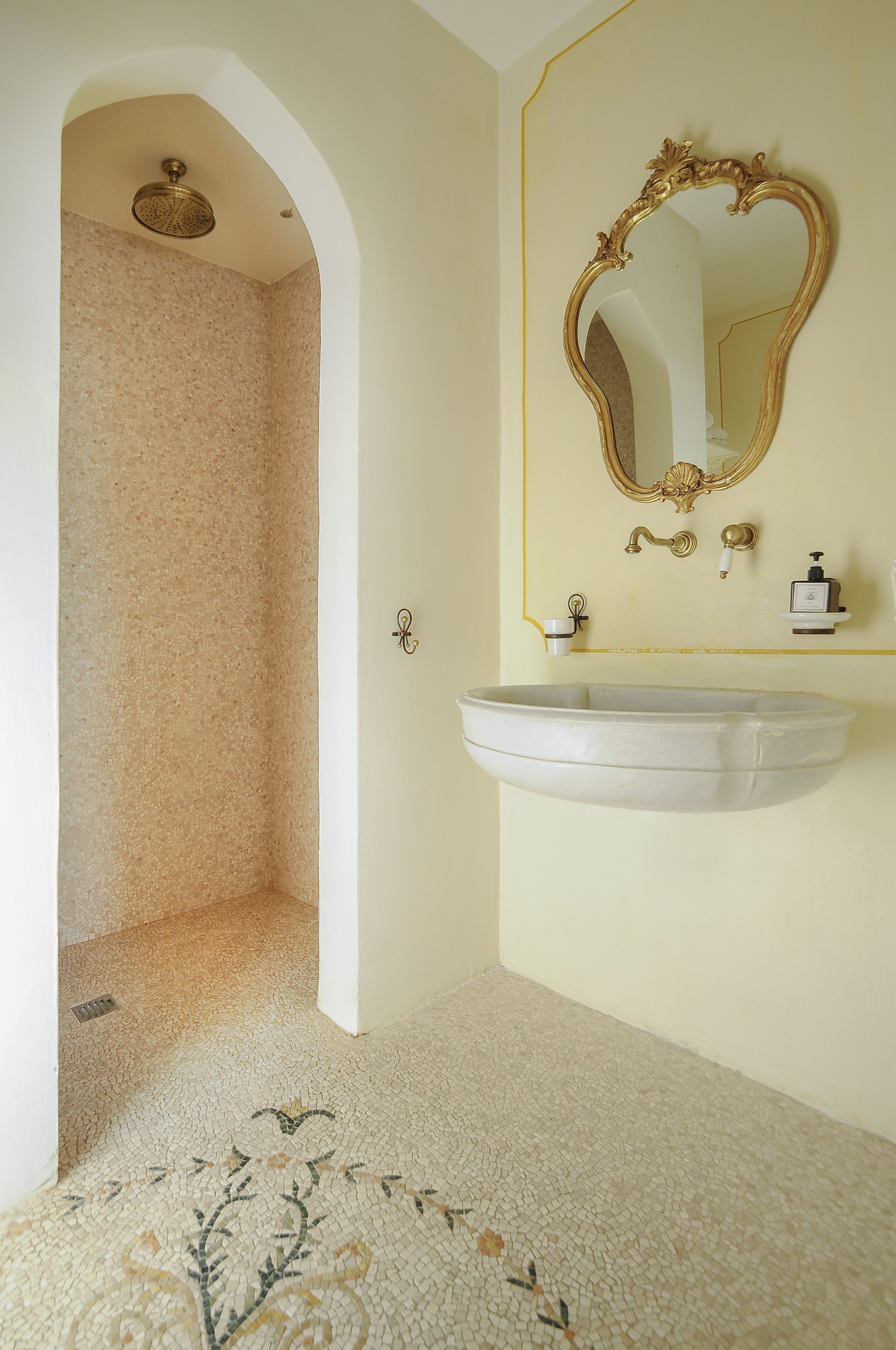 A bathroom with a freestanding sink, a mirror with an ornate frame, and a shower area with a textured wall.