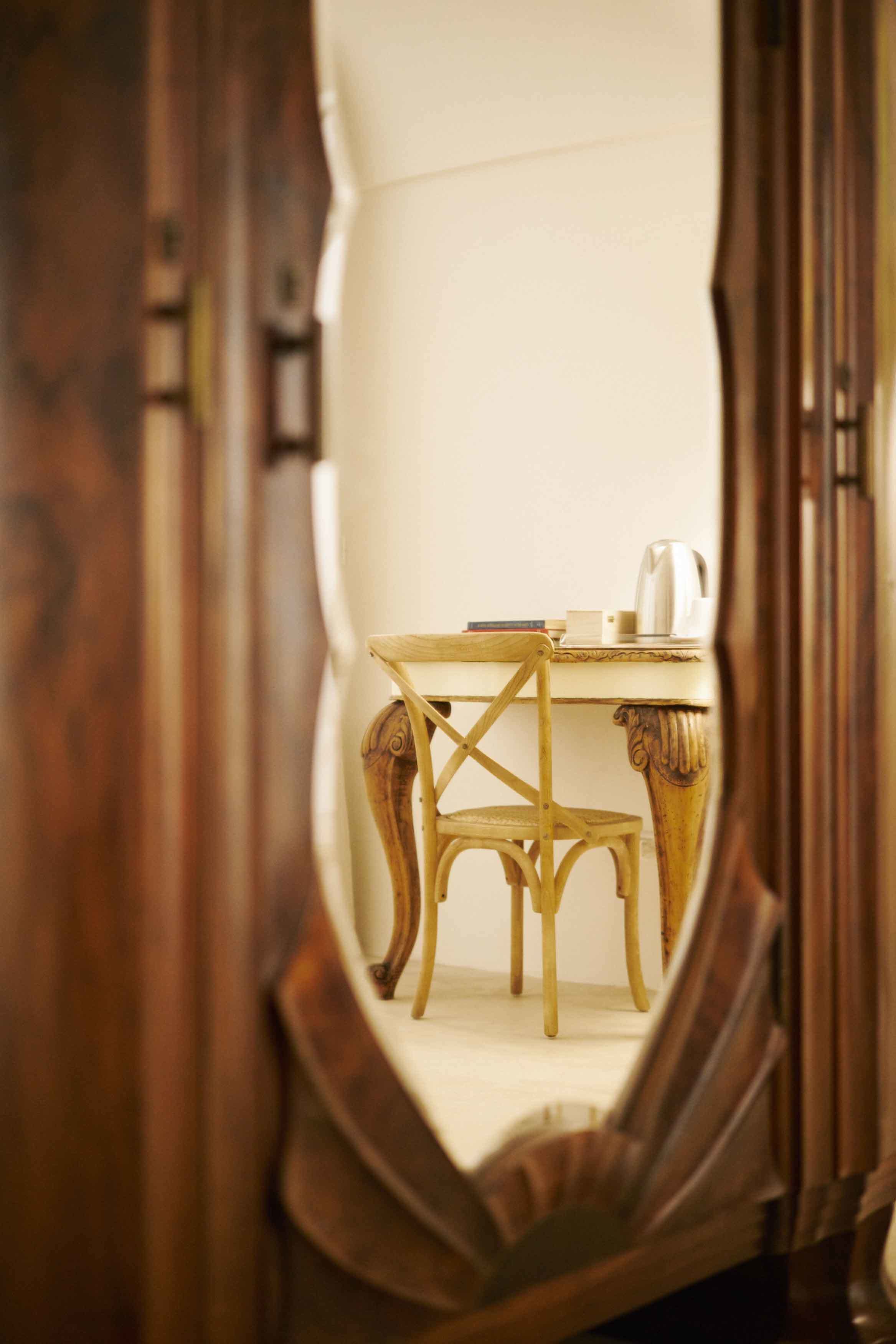 Un espejo que refleja una silla de madera y una mesita con un hervidor.