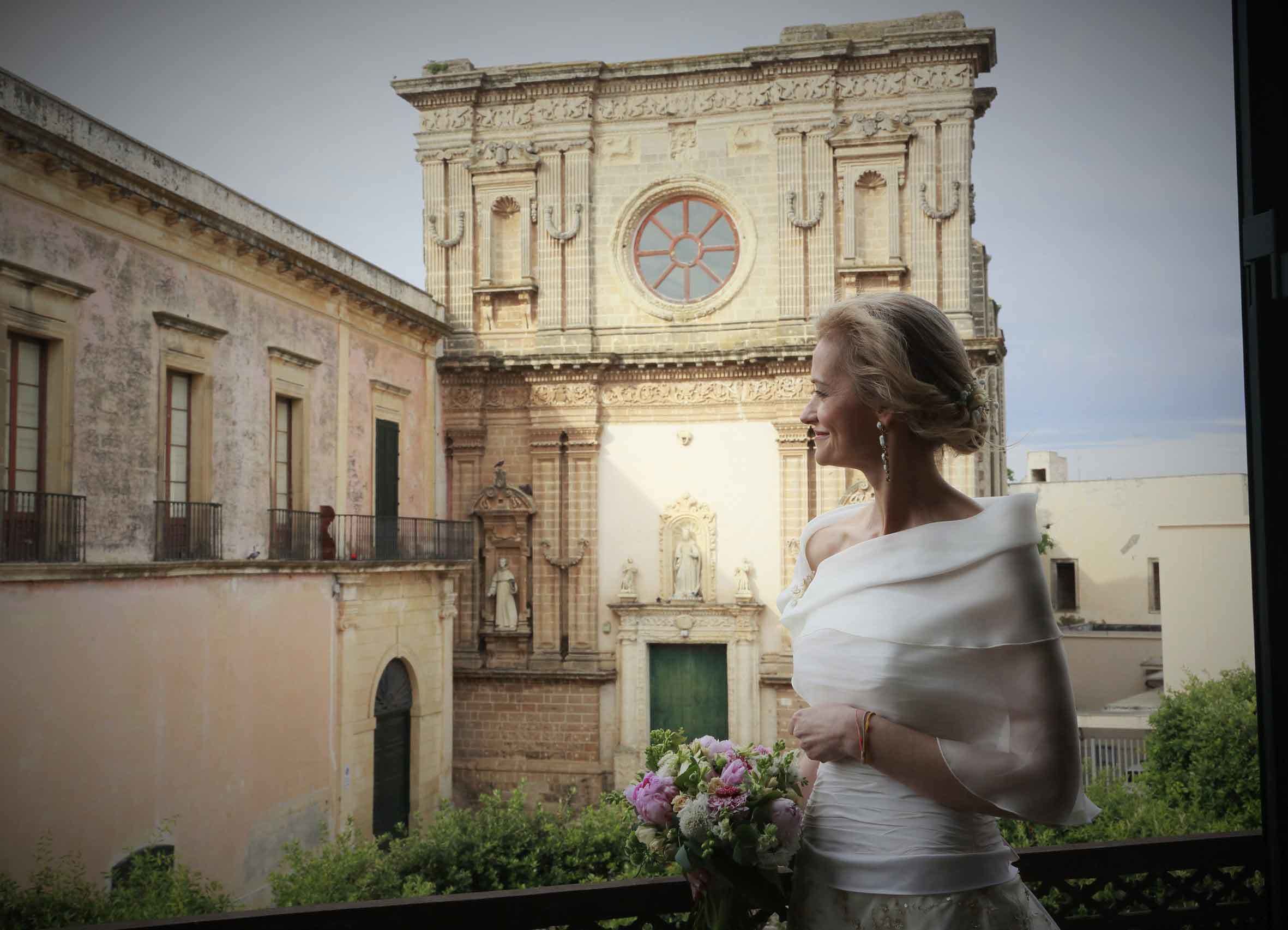 Una mujer sostiene un ramo de flores frente a un edificio histórico con un gran ventanal circular y estatuas.
