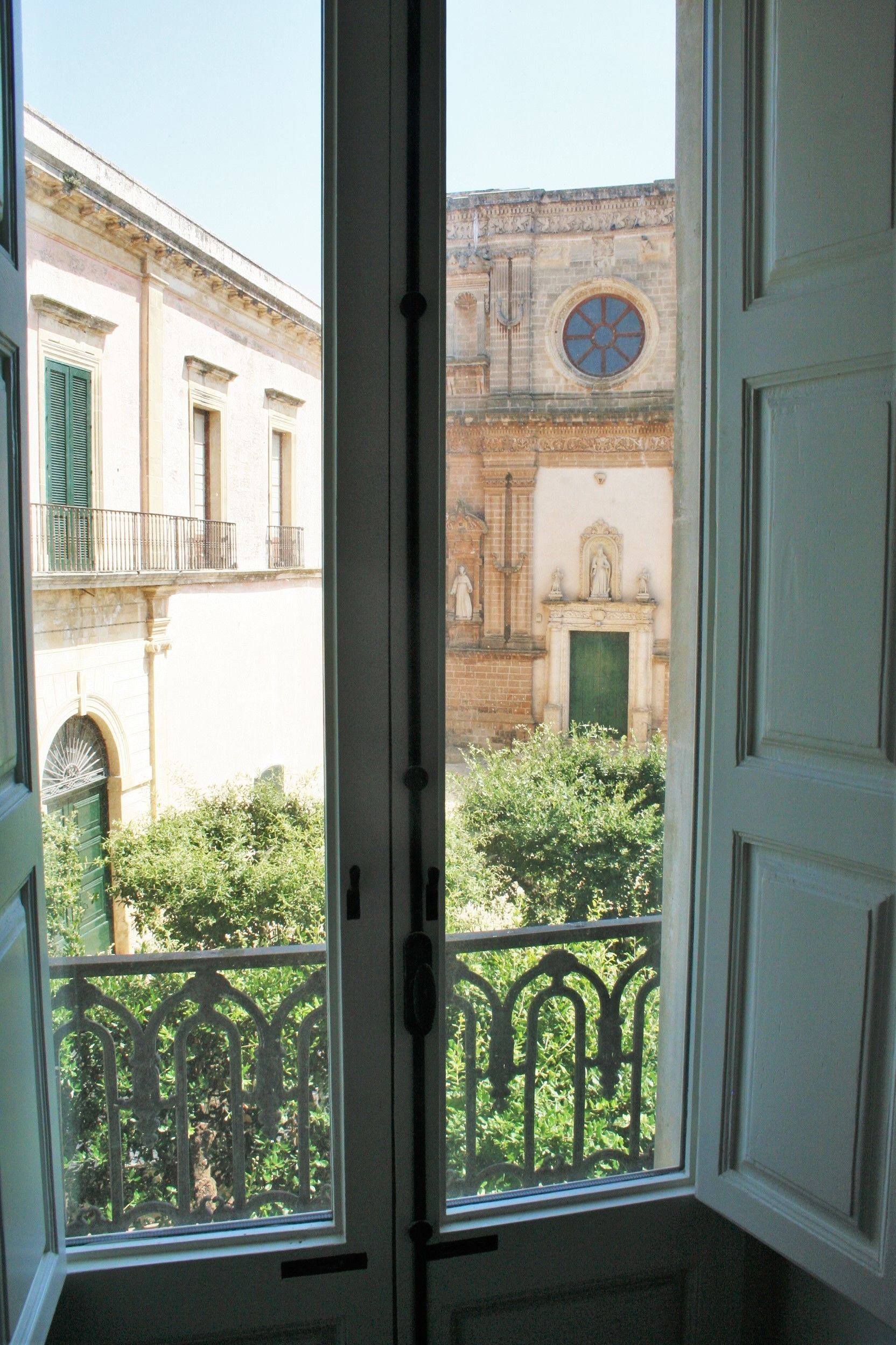 A view from a balcony with a wrought iron railing, overlooking a building with a round window and a statue.