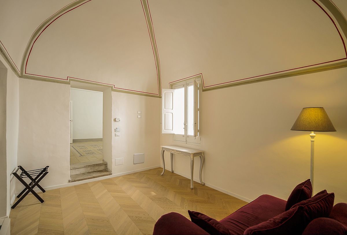 Una habitación con suelo de parqué de madera, un sofá rojo, una consola blanca y una lámpara.