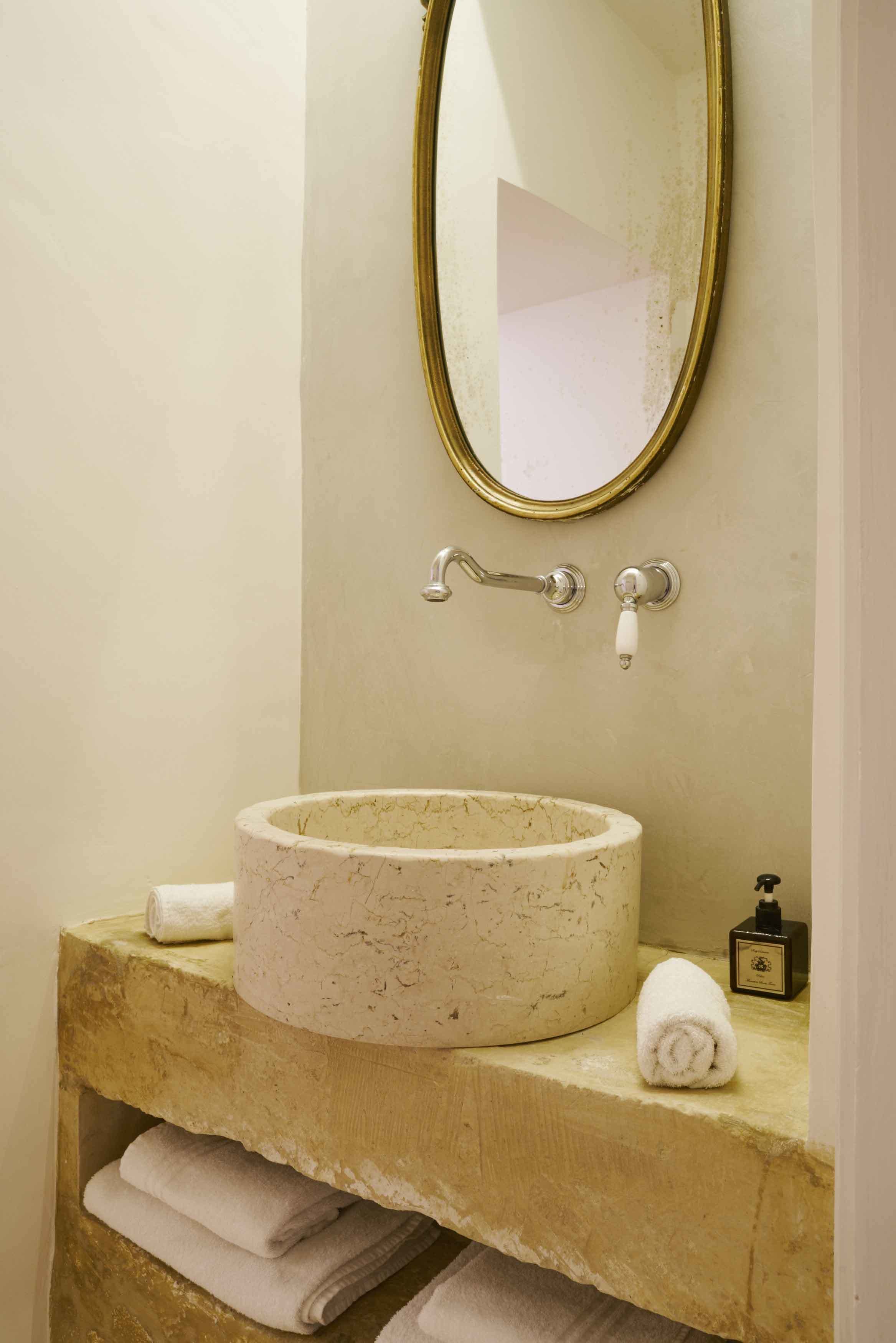 Une salle de bain avec un lavabo en marbre, un miroir encadré d’or et un porte-serviettes.