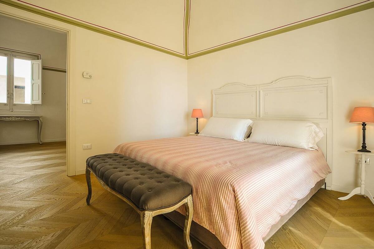Una camera da letto con un letto grande, una panca, due lampade da comodino e una finestra.