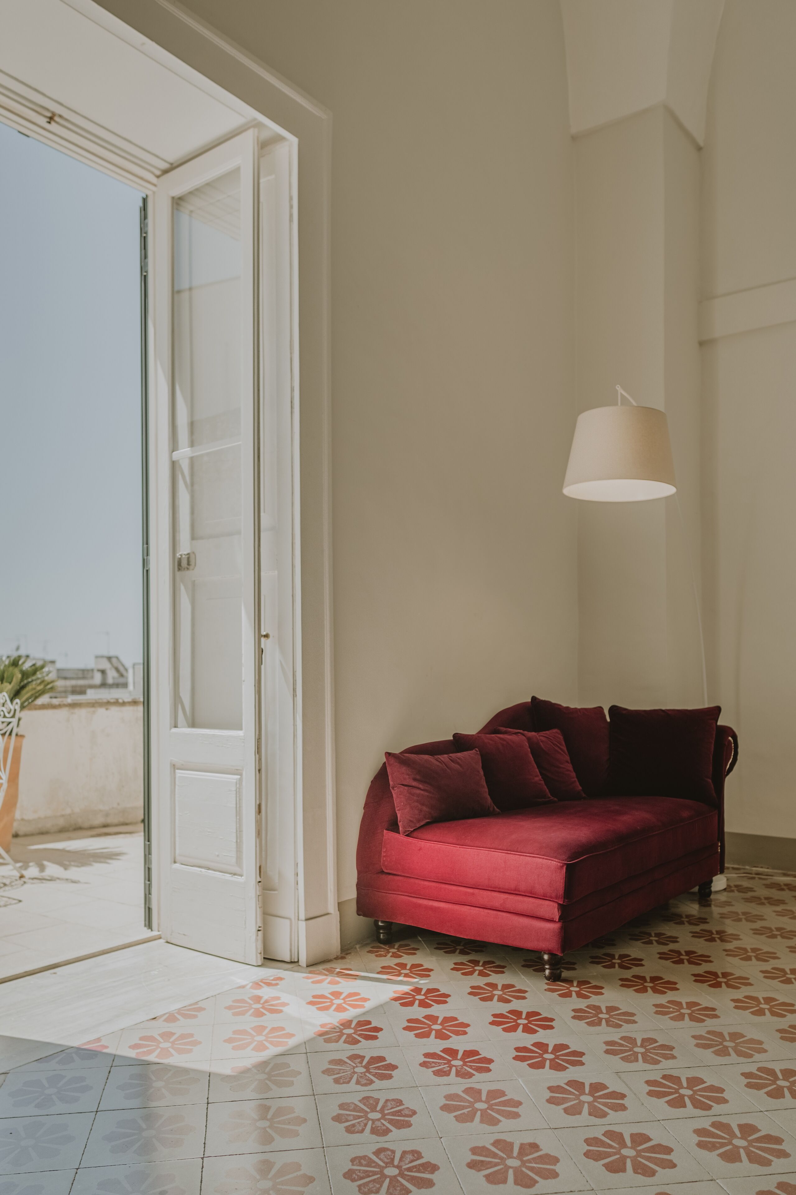 A red sofa in a room with a patterned floor, a white door, and a hanging light fixture.