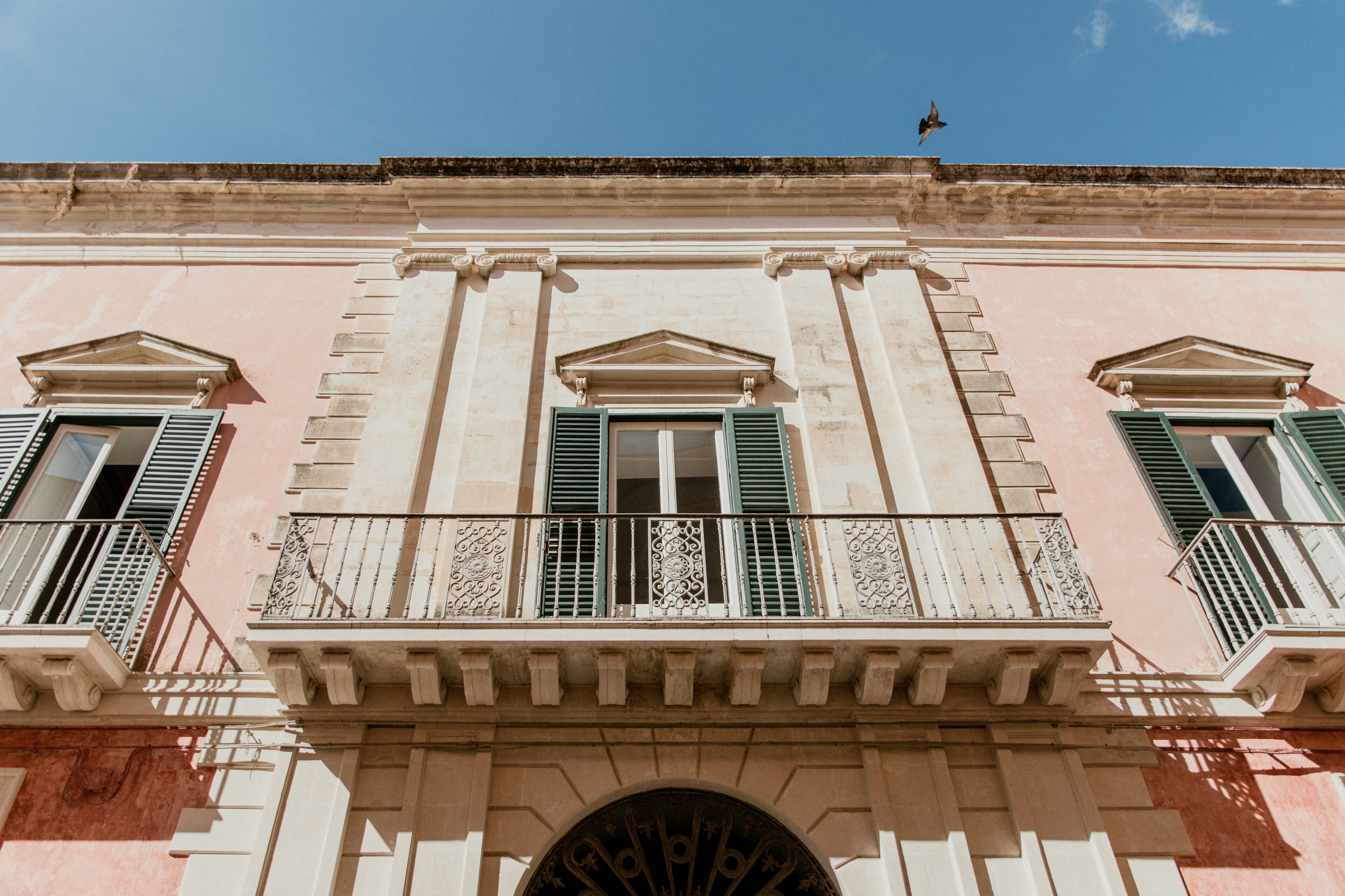 A building facade with three windows, each with green shutters and decorative railings.