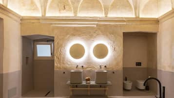 Une salle de bain spacieuse avec une grande baignoire, un grand miroir rond et deux lavabos.