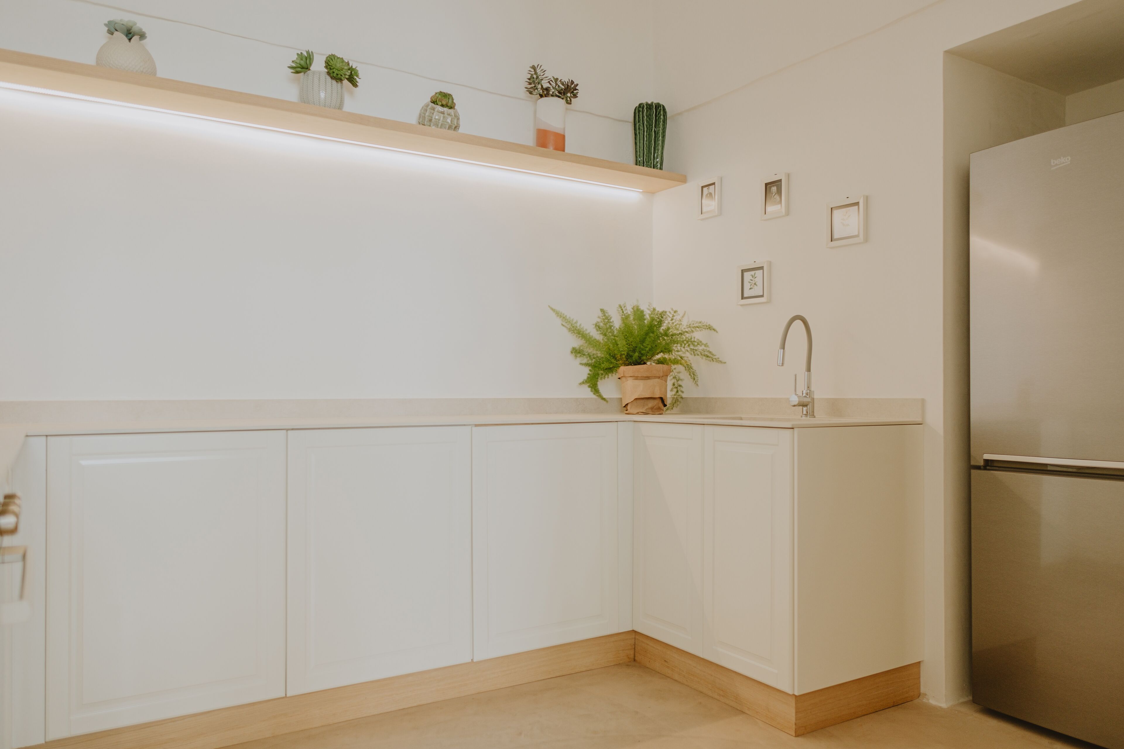 Een moderne keuken met witte kastjes, een roestvrijstalen koelkast, een houten aanrecht en een plank met decoratieve planten.