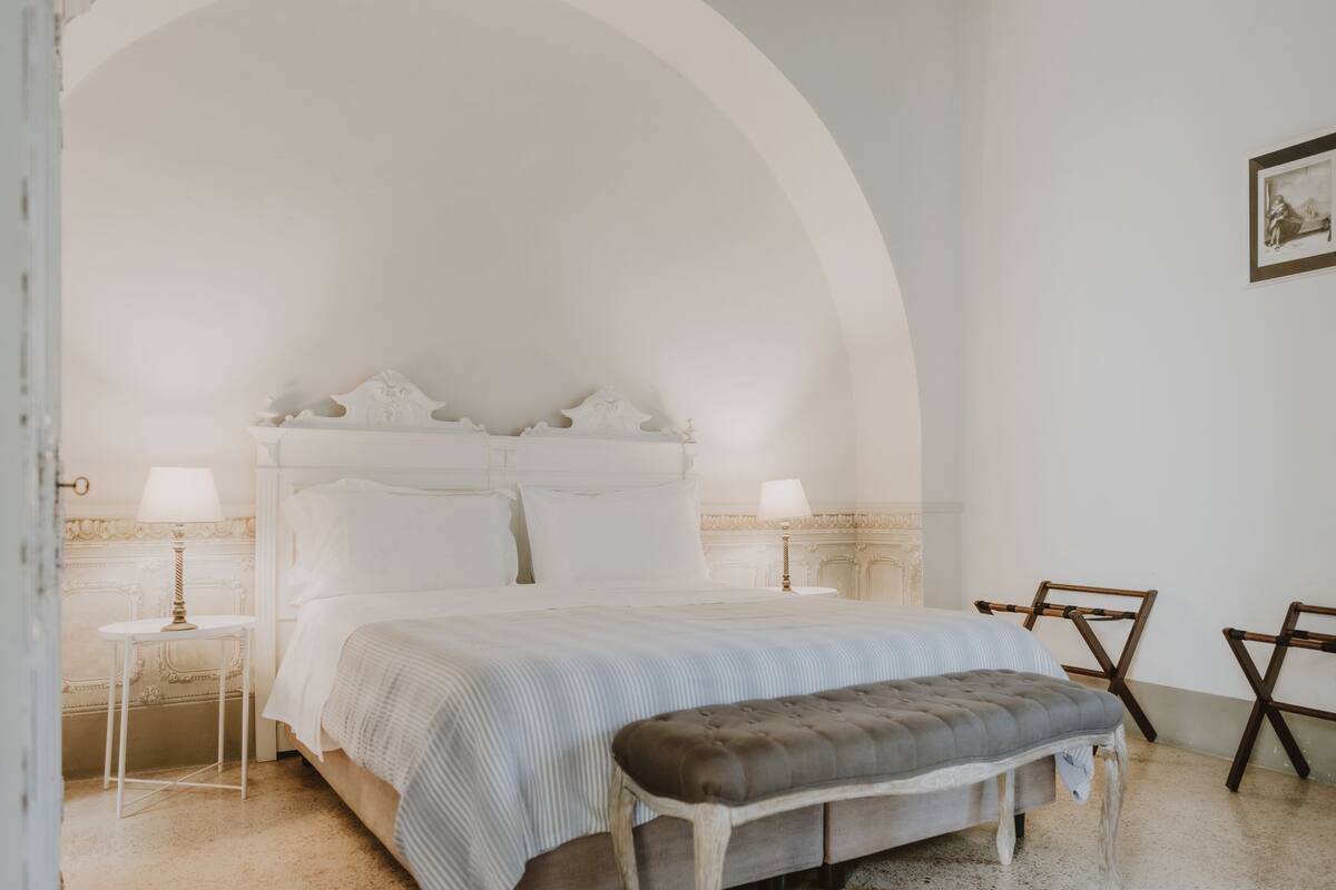 Una camera da letto con un letto grande, due comodini, una panca e una sedia.