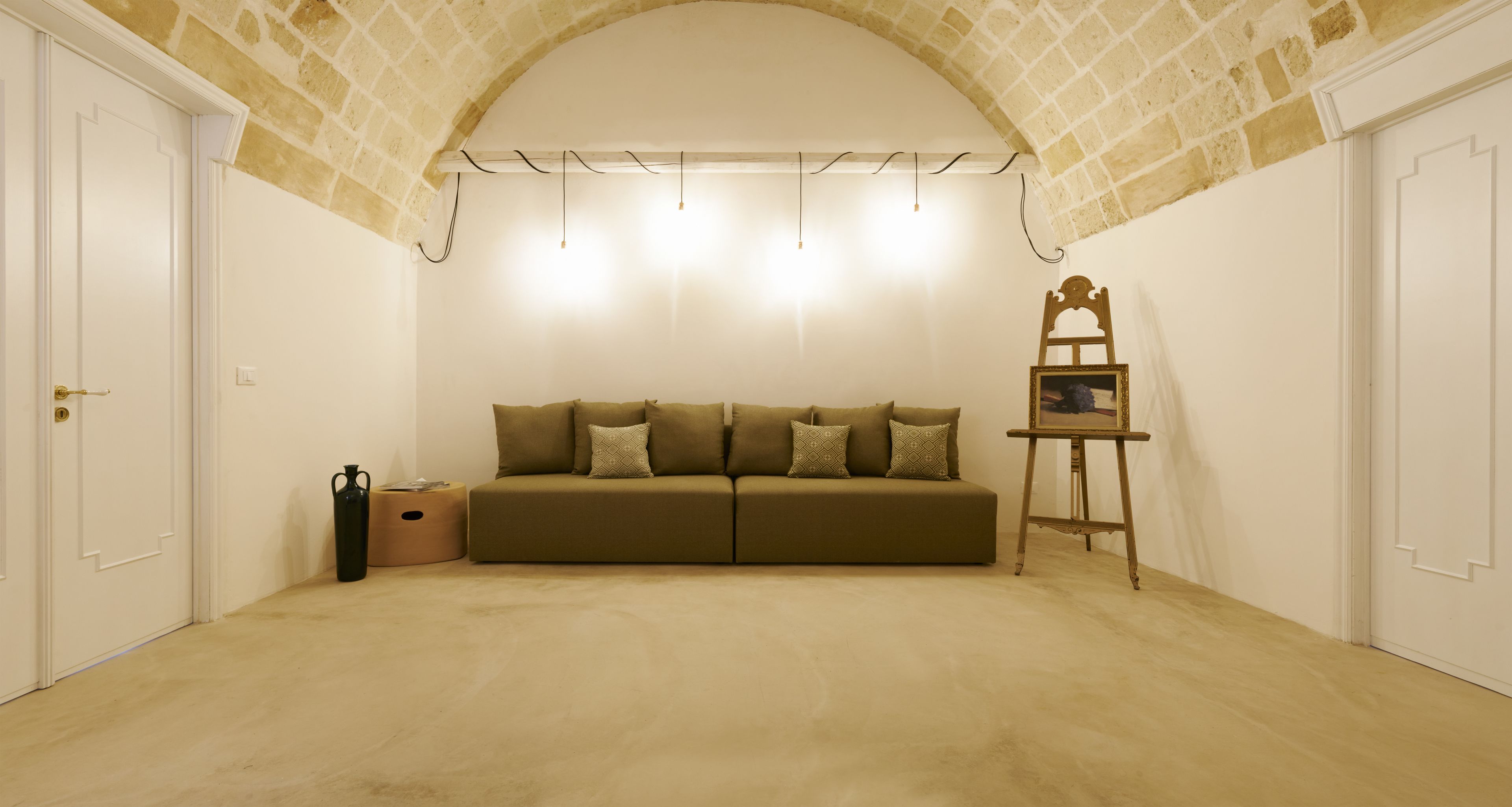 Una habitación con alfombra color beige, un sofá color beige con cojines estampados, una escalera de madera con un cuadro, y puertas blancas.